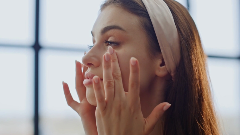 Žena prstima nanosi proizvod za negu na lice ispred ogledala