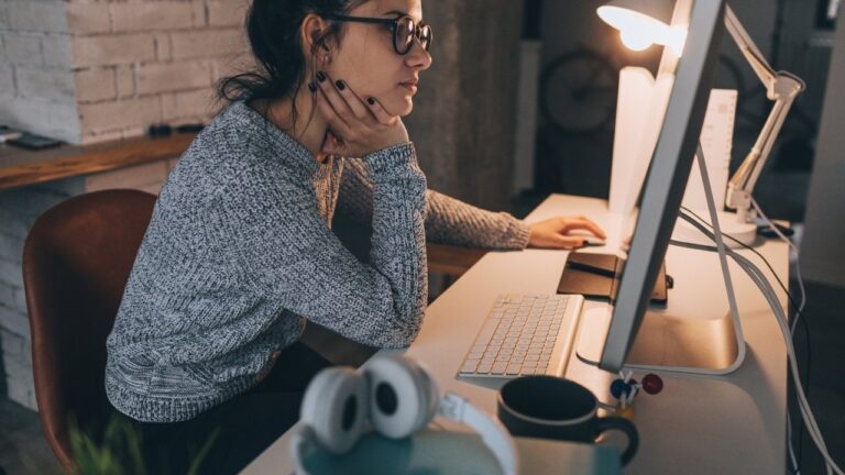 Programerka sedi za računarom u pogrbljenom položaju tokom dugog radnog dana.